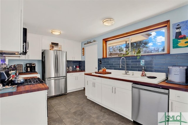 kitchen featuring decorative backsplash, butcher block countertops, stainless steel appliances, white cabinetry, and a sink