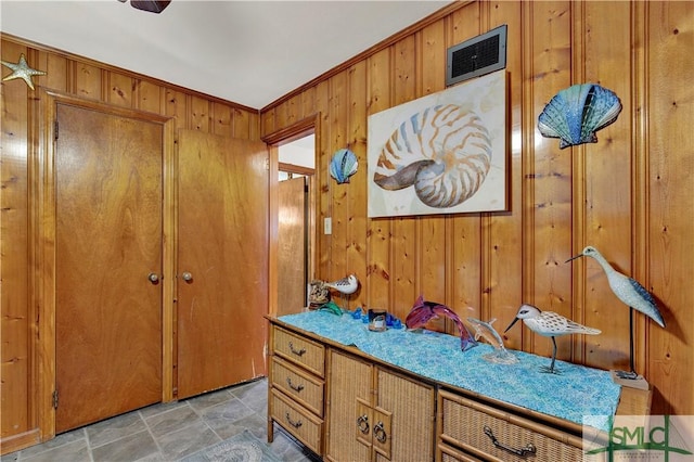 bathroom with stone finish flooring, ornamental molding, visible vents, and wooden walls