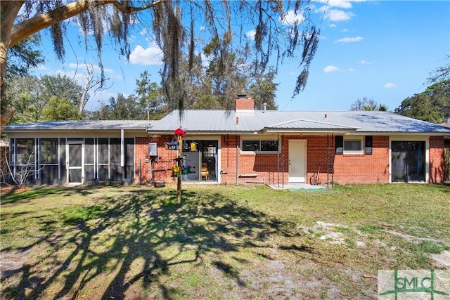 back of house featuring a sunroom, a chimney, brick siding, and a yard