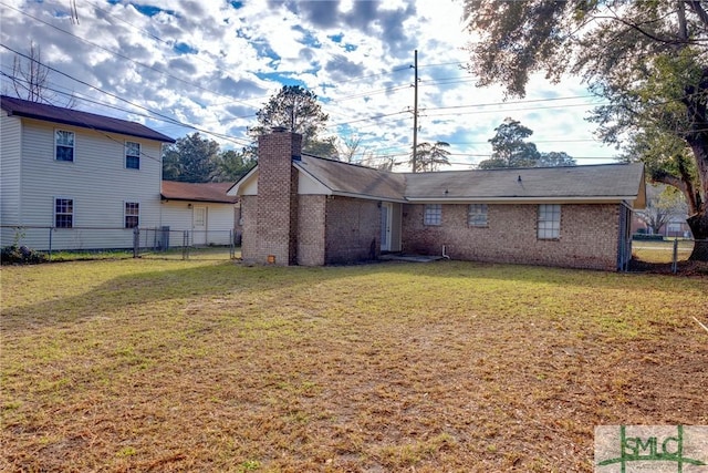 rear view of property with brick siding, a lawn, a chimney, and fence