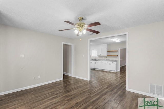 unfurnished living room with ceiling fan, a textured ceiling, dark wood-style flooring, visible vents, and baseboards