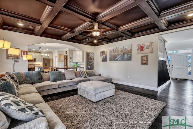 living area featuring arched walkways, ceiling fan with notable chandelier, dark wood-type flooring, baseboards, and ornamental molding