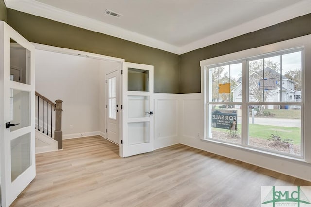 interior space featuring light wood-style flooring, a decorative wall, a wainscoted wall, visible vents, and stairs