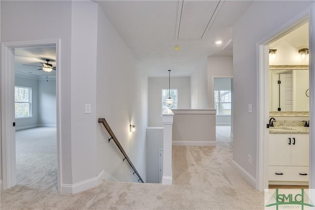 corridor with light colored carpet, a sink, an upstairs landing, baseboards, and attic access