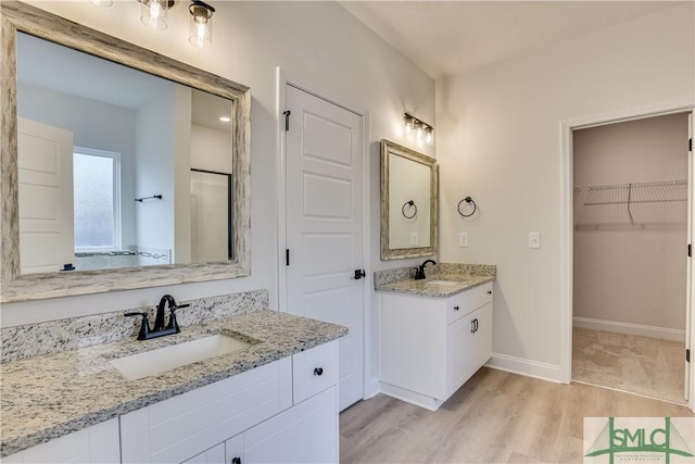 full bath with wood finished floors, two vanities, a sink, and baseboards