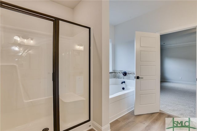 bathroom featuring wood finished floors, a shower stall, a bath, and baseboards