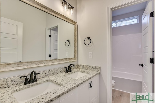 full bathroom with double vanity, wood finished floors, a sink, and toilet