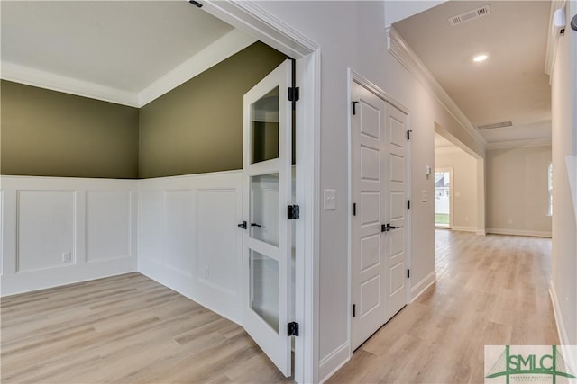 corridor featuring a decorative wall, light wood-type flooring, visible vents, and crown molding