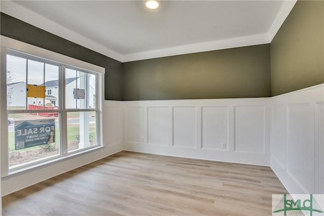 unfurnished room featuring crown molding, a decorative wall, wainscoting, and light wood-style floors