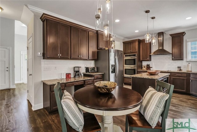 kitchen with appliances with stainless steel finishes, dark brown cabinetry, wall chimney range hood, and ornamental molding