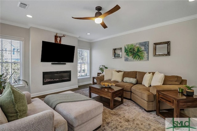 living room with ceiling fan, visible vents, baseboards, a glass covered fireplace, and crown molding