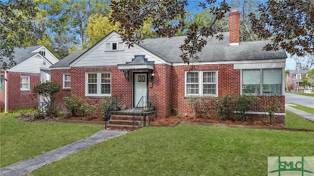 view of front of house with a shingled roof, a chimney, a front lawn, and brick siding