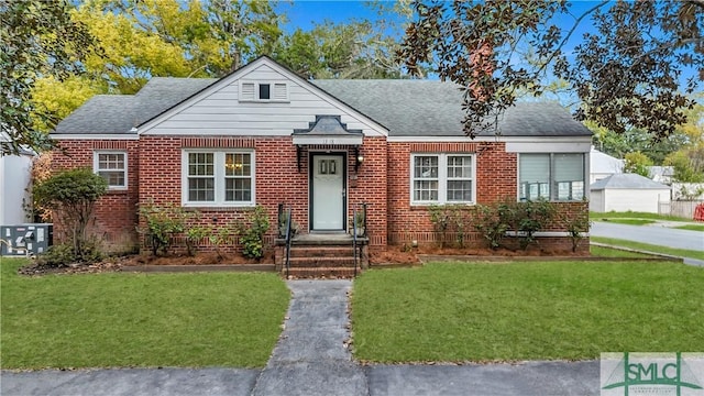 bungalow with roof with shingles, central AC unit, a front lawn, and brick siding