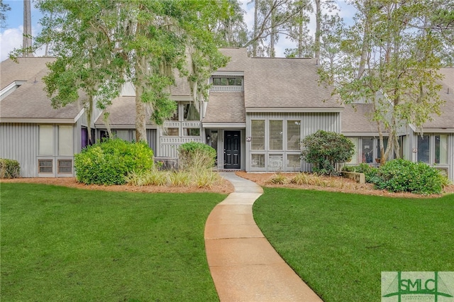 view of front facade with roof with shingles and a front yard