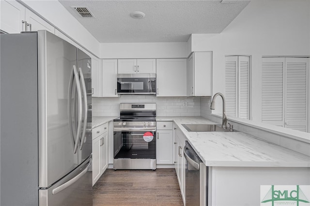 kitchen featuring stainless steel appliances, visible vents, dark wood-type flooring, white cabinets, and a sink