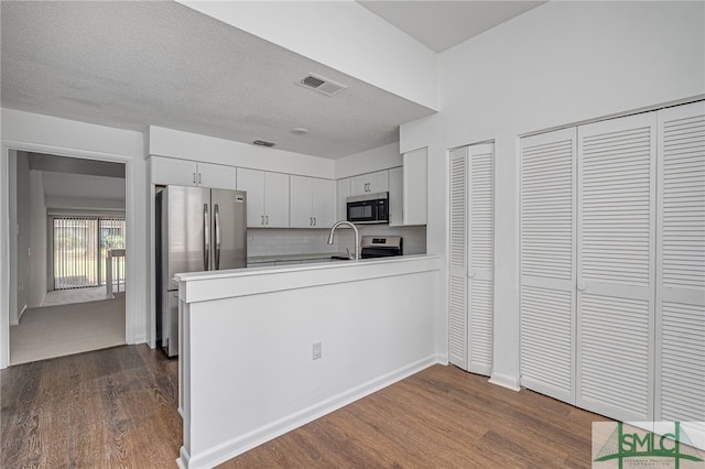 kitchen featuring dark wood-style flooring, light countertops, visible vents, appliances with stainless steel finishes, and a peninsula