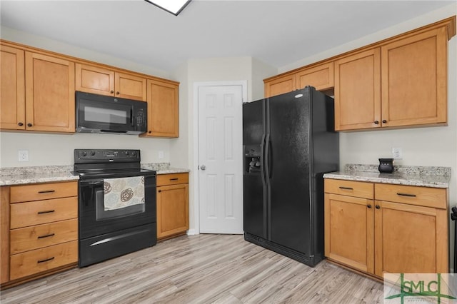 kitchen featuring light wood-style flooring, black appliances, and light stone countertops