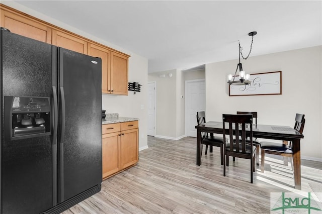 kitchen with a chandelier, baseboards, light wood-style floors, black refrigerator with ice dispenser, and decorative light fixtures