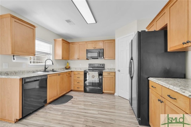 kitchen with visible vents, light wood-style flooring, a sink, light stone countertops, and black appliances