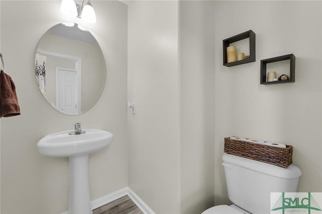 half bathroom with wood finished floors, toilet, and baseboards