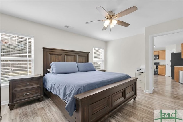 bedroom featuring light wood finished floors, visible vents, a ceiling fan, freestanding refrigerator, and baseboards