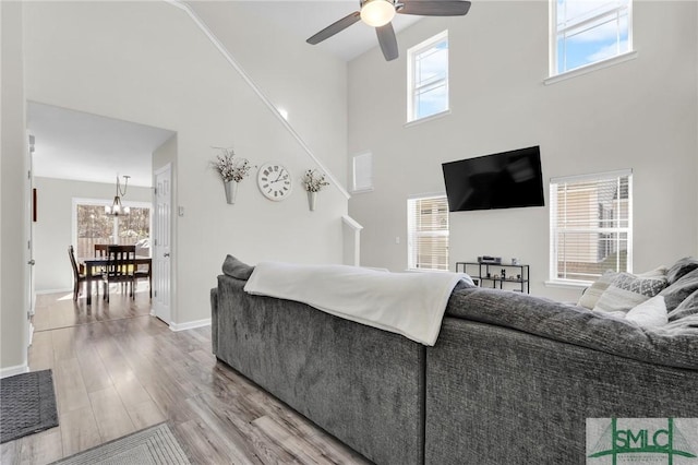 living area with light wood-type flooring, ceiling fan, a high ceiling, and baseboards