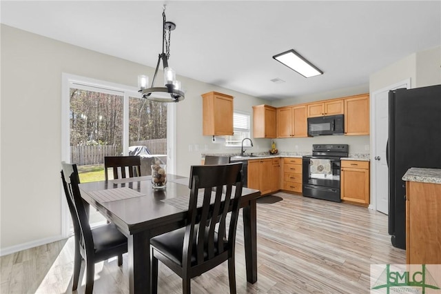 interior space featuring a sink, hanging light fixtures, light countertops, black appliances, and light wood finished floors