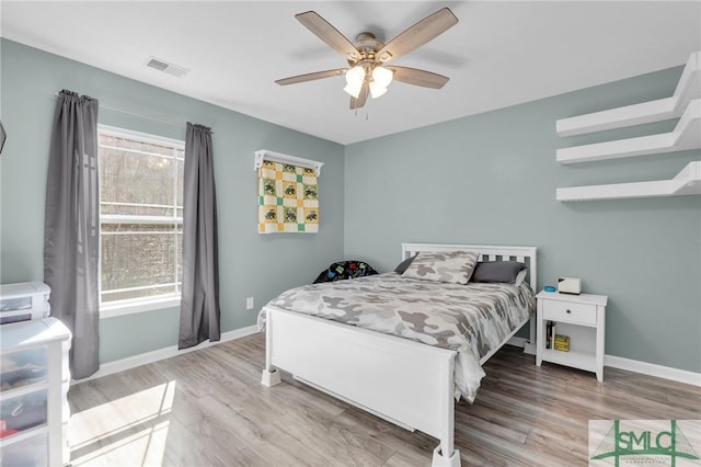 bedroom featuring a ceiling fan, visible vents, baseboards, and wood finished floors