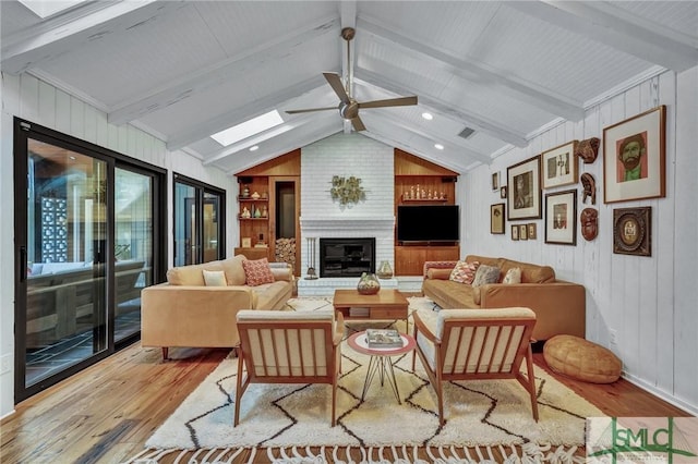 living room with visible vents, a ceiling fan, lofted ceiling with skylight, wood finished floors, and a fireplace