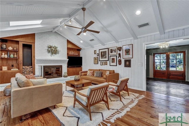 living area featuring visible vents, wood finished floors, vaulted ceiling with beams, french doors, and a brick fireplace