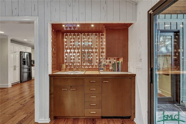 bar featuring a sink, wood finished floors, stainless steel fridge, and wet bar