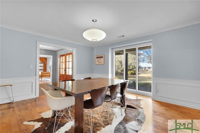 dining area with a wainscoted wall, visible vents, light wood finished floors, and ornamental molding