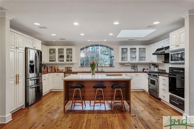 kitchen featuring a breakfast bar, stainless steel appliances, white cabinetry, light wood-type flooring, and under cabinet range hood