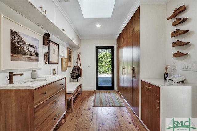 doorway to outside with a skylight, crown molding, recessed lighting, a sink, and light wood-type flooring