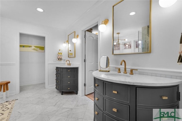 bathroom with a wainscoted wall, marble finish floor, two vanities, and a sink