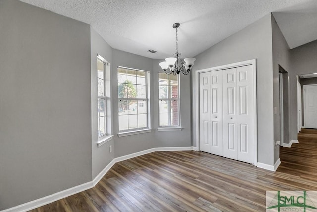 unfurnished dining area with visible vents, vaulted ceiling, wood finished floors, a chandelier, and baseboards