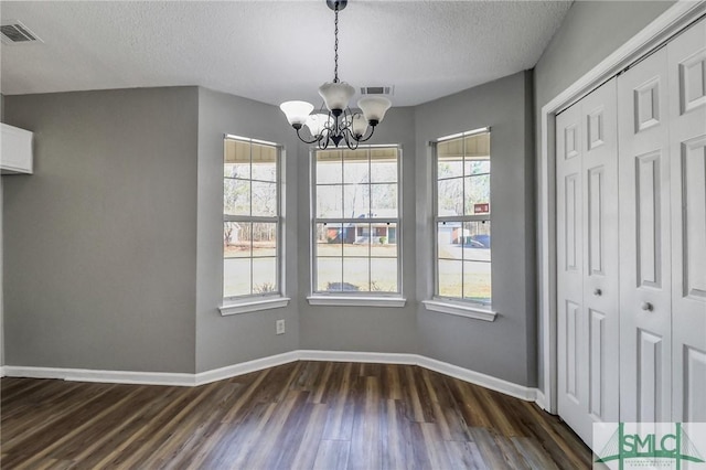 unfurnished dining area featuring dark wood-style floors, a notable chandelier, visible vents, and baseboards