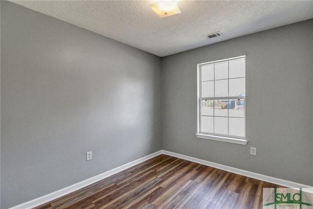 empty room with baseboards, visible vents, dark wood finished floors, and a textured ceiling