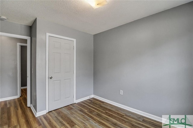 unfurnished bedroom with a textured ceiling, baseboards, and wood finished floors