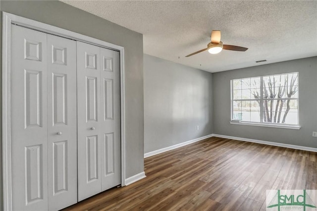 unfurnished bedroom with dark wood-style floors, a textured ceiling, baseboards, and a closet