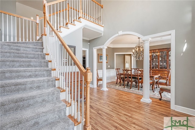 staircase with decorative columns, crown molding, arched walkways, and wood finished floors