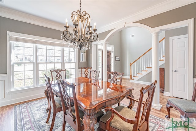 dining area with arched walkways, light wood-style floors, stairs, decorative columns, and crown molding