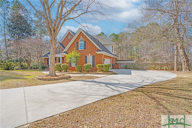 traditional-style house featuring brick siding, fence, a garage, driveway, and a front lawn