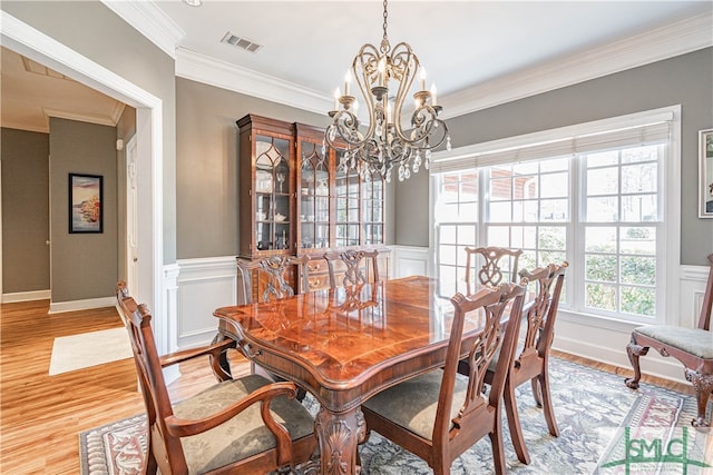 dining room with visible vents, a wainscoted wall, ornamental molding, light wood-style floors, and a chandelier