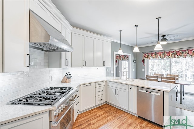 kitchen with wall chimney range hood, white cabinetry, appliances with stainless steel finishes, and a sink