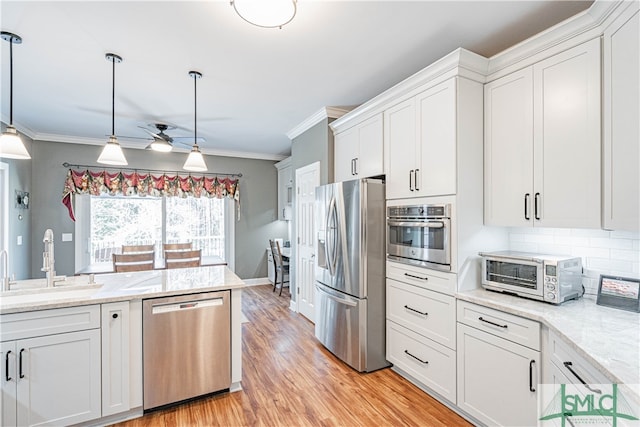 kitchen featuring light wood-style flooring, stainless steel appliances, a sink, white cabinets, and decorative backsplash