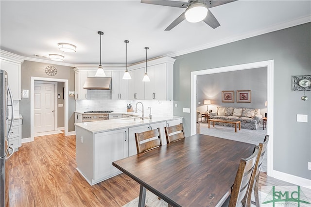 kitchen with under cabinet range hood, a peninsula, a sink, tasteful backsplash, and crown molding