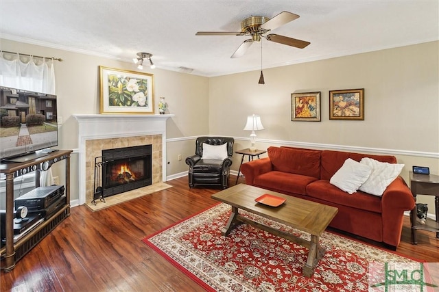 living area featuring a ceiling fan, crown molding, a tiled fireplace, and wood finished floors