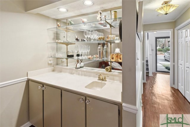 bar with ornamental molding, wood finished floors, and a sink