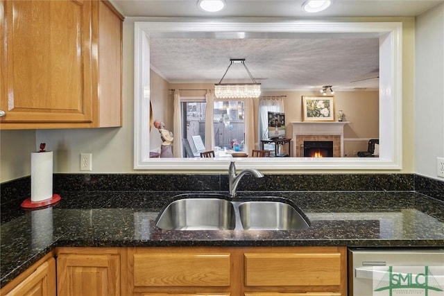 kitchen with a fireplace, stainless steel dishwasher, a sink, a textured ceiling, and dark stone countertops